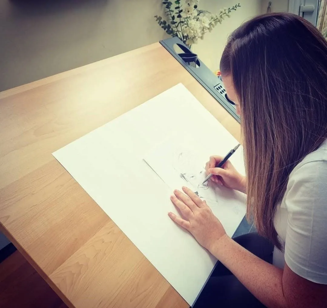 Sarah Kerry of Sarah Mallett Portraits drawing a pencil portrait commission at her desk in Devon